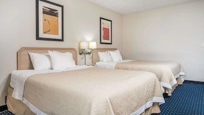 Habitació d'hotel amb dos llits, cadascun amb un llençol color beix i almoines blanques. Hi ha dues làmpades muntades a la paret, a cada banda dels llits.
