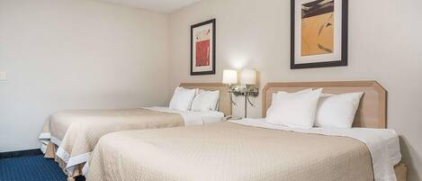 A hotel room with two beds, each with a beige bedspread and white pillows. There are two wall-mounted lamps on either side of the beds.