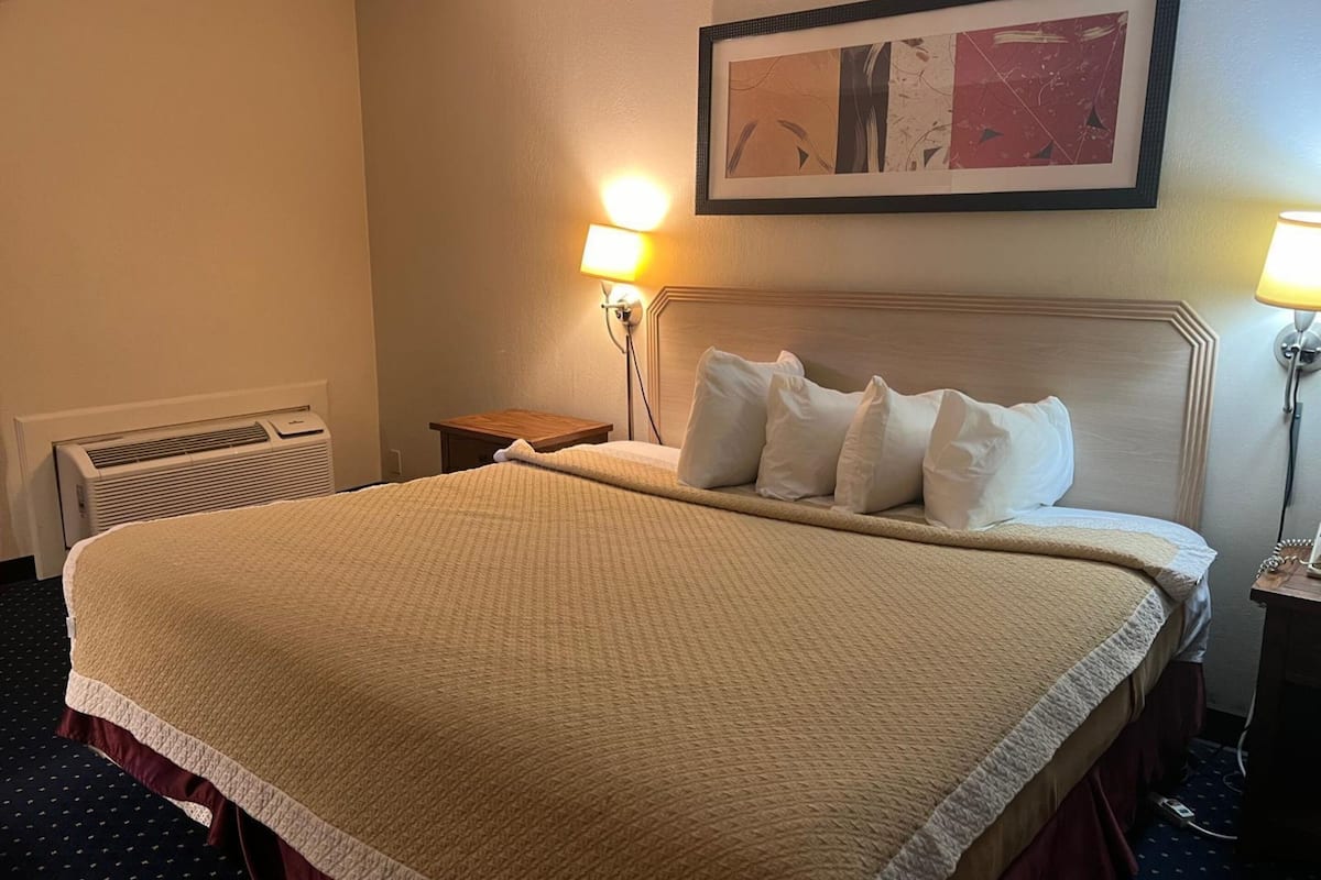 Ein Hotelzimmer mit einem großen Bett, zwei Nachttischlampen, einem gerahmten Kunstwerk an der Wand und einem Heizkörper am Boden.