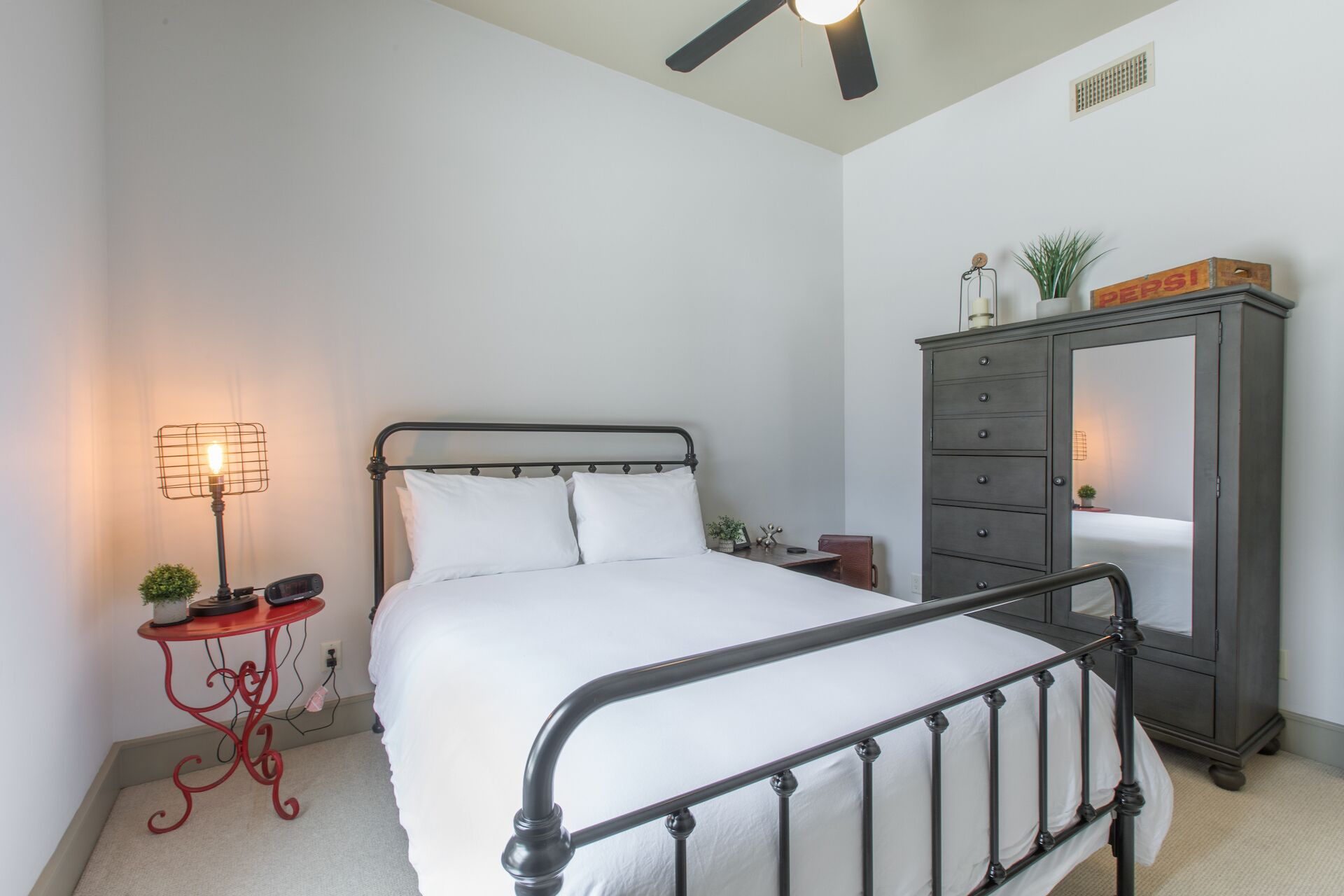 A bedroom with a bed, a nightstand, a lamp, a dresser, and a ceiling fan.