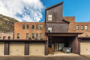 A modern building with a garage entrance, a staircase leading to a second floor, and a mountain backdrop.