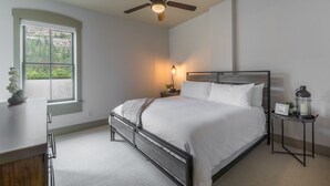 A bedroom with a bed, a ceiling fan, a bedside table with a lamp, and a window with a view of greenery. - Contemporary Cozy Loft | Heart of Downtown | Air Conditioning (Ouray)