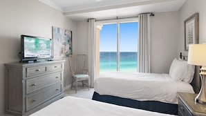 Ein Hotelzimmer mit zwei Betten, einem Fernseher, einem Sessel und Blick auf den Ozean.