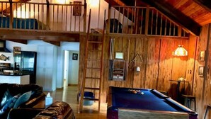 A cozy living room with a pool table, a leather couch, and a wooden staircase. - Rustic newly remodeled River House on working fish house property . Gulf access (Inglis)