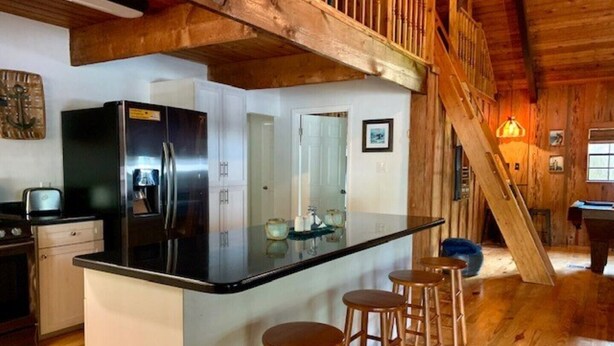 A kitchen with a central island, wooden bar stools, and a staircase leading to an upper level. - Rustic newly remodeled River House on working fish house property . Gulf access (Inglis)