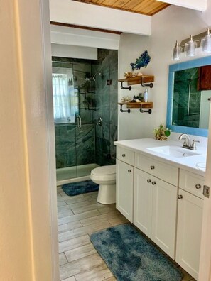 A modern bathroom with a glass shower enclosure, white cabinetry, and a blue accent rug.