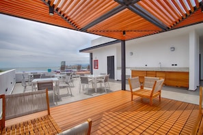 Una terraza en la azotea con suelo de madera, mobiliario exterior, una zona de cocina y vistas al mar.