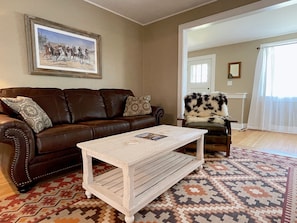 A living room with a brown leather sofa, a white coffee table, and a patterned rug. - The Buckaroo- walk to historic downtown Cody, dog friendly! (Cody)