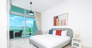 A modern bedroom with a large bed, a view of the city, and a balcony with a chair and plant. - LUX - Opulent Island Suite 6 (Dubai)