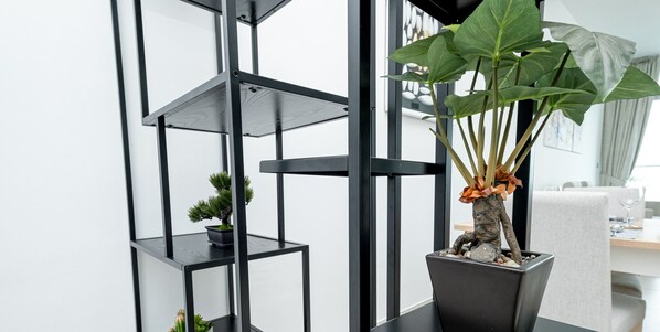 A modern interior with a black metal shelving unit, a potted plant, and a dining area with a white table and chairs. - LUX - Opulent Island Suite 6 (Dubai)