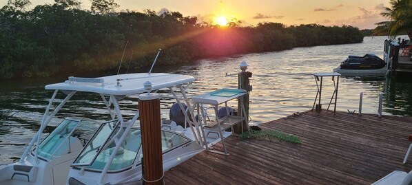 A boat docked at a wooden pier with a view of the sunset over a river. - Tiny home in Key Largo with Private Dock, Tiki Hut and Boat Lift (Key Largo)