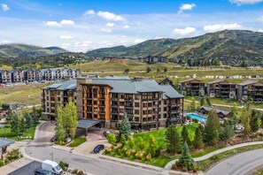 A multi-story hotel with a pool, surrounded by greenery and mountains. - First Tracks 3105 1 Bedroom Condo by RedAwning (Steamboat Springs)