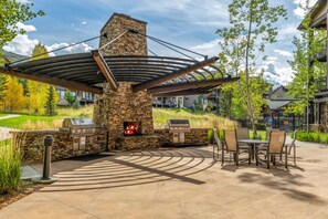 An outdoor patio with a stone fireplace, grilling area, and seating. - First Tracks 3105 1 Bedroom Condo by RedAwning (Steamboat Springs)