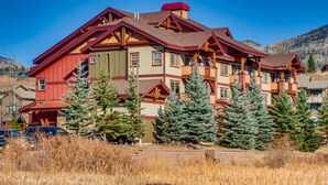 Un chalet à étages, à la façade rouge et beige, doté de balcons en bois et surplombant un paysage montagneux.