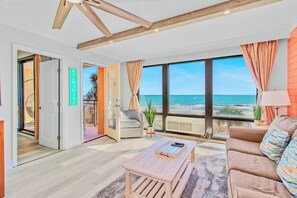A spacious living room with a large window overlooking the beach, a cozy seating area, and a wooden coffee table. - RARE JACUZZI HONEYMOON CONDO/1000SQFT/2BATH/SWING (Myrtle Beach)