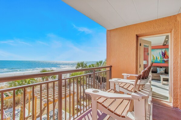 A balcony with a view of the beach, wooden chairs, and a table. - RARE JACUZZI HONEYMOON CONDO/1000SQFT/2BATH/SWING (Myrtle Beach)