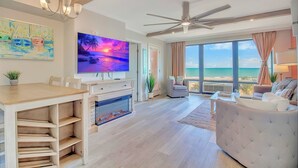 Uma sala de estar ampla com uma televisão grande, lareira e vista para o oceano.