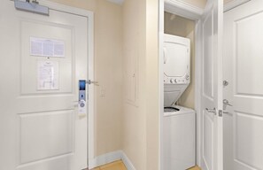 Un pasillo con una puerta a la izquierda, un cuarto de lavado con lavadora y secadora, y una puerta blanca a la derecha.