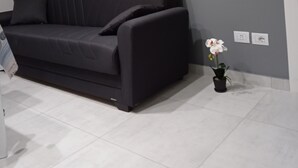 A modern living room with a dark grey sofa, a small potted orchid, and a wall-mounted 'HELIO' sign. - Regis Apartament (Milazzo)