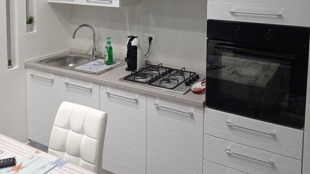 A modern kitchen with white cabinets, a stainless steel sink, a gas stove, and a black oven. - Regis Apartament (Milazzo)