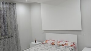 A modern bedroom with a bed, a nightstand, a wall-mounted TV, and a decorative curtain. - Regis Apartament (Milazzo)