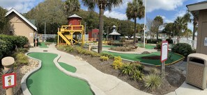 A miniature golf course with a red tower, a white fence, and a 'Welcome' sign.