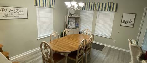 A dining room with a wooden table and chairs, a chandelier, and a sign that reads "Bless."
