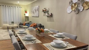Un coin repas avec une table en bois dressée pour six personnes, entourée de chaises recouvertes d’un tissu gris.