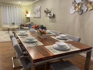 Uma sala de jantar com uma mesa de madeira posta para seis pessoas, rodeada por cadeiras estofadas cinzentas.