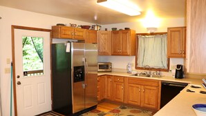 A compact kitchen with wooden cabinets, a stainless steel refrigerator, a microwave, and a dishwasher. - Cozy Home Away from Home. Sleeps 12! (Sugar Mountain)