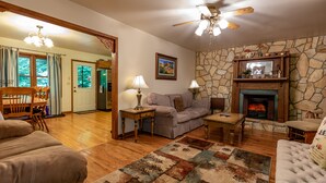 A cozy living room with a fireplace, wooden furniture, and a stone wall. - Cozy Home Away from Home. Sleeps 12! (Sugar Mountain)