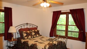 A bedroom with a bed, a nightstand, a lamp, a ceiling fan, and a window with curtains. - Cozy Home Away from Home. Sleeps 12! (Sugar Mountain)