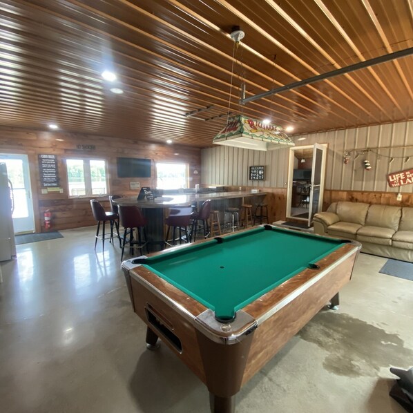 A pool table in a room with wooden walls and ceiling, a bar area, and a sofa. - The Musky Cabin on the Big Eau Pleine Reservoir! (Auburndale)
