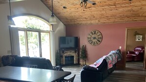 A spacious living room with a large wooden ceiling, a fireplace, a clock, and a cozy seating area. - The Musky Cabin on the Big Eau Pleine Reservoir! (Auburndale)