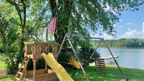 A wooden play structure with a slide, a swing set, and an American flag. - The Musky Cabin on the Big Eau Pleine Reservoir! (Auburndale)