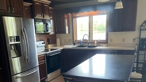A kitchen with a stainless steel refrigerator, an oven, a sink, and a large island with chairs. - The Musky Cabin on the Big Eau Pleine Reservoir! (Auburndale)
