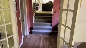 A staircase leading to a room with a window, a door with a glass panel, and a small seating area with a couch and a chair. - Home in the woods - Big, Acreage, Nature Oasis, King Bed, Giant Windows (Monson)