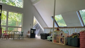A room with large windows, a loft area with a playhouse, and a table with chairs. - Home in the woods - Big, Acreage, Nature Oasis, King Bed, Giant Windows (Monson)