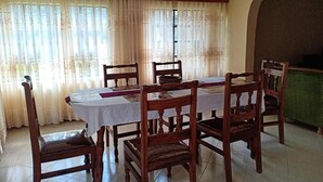 Un coin repas comprenant une table et six chaises en bois, une fenêtre avec des rideaux et un mur vert.