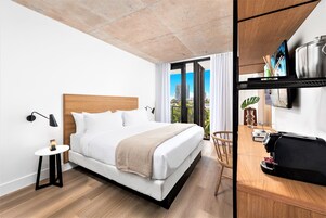 A modern hotel room with a large bed, a small side table, a desk with a laptop, and a view of the city.