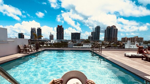 A pool area with a city skyline view, lounge chairs, and a wooden deck. - UPSUN HOTEL (Miami Beach)