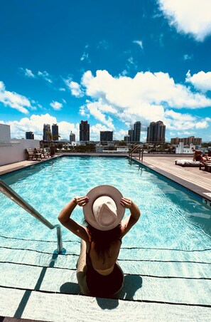 A pool area with a city skyline view, lounge chairs, and a wooden deck. - UPSUN HOTEL (Miami Beach)