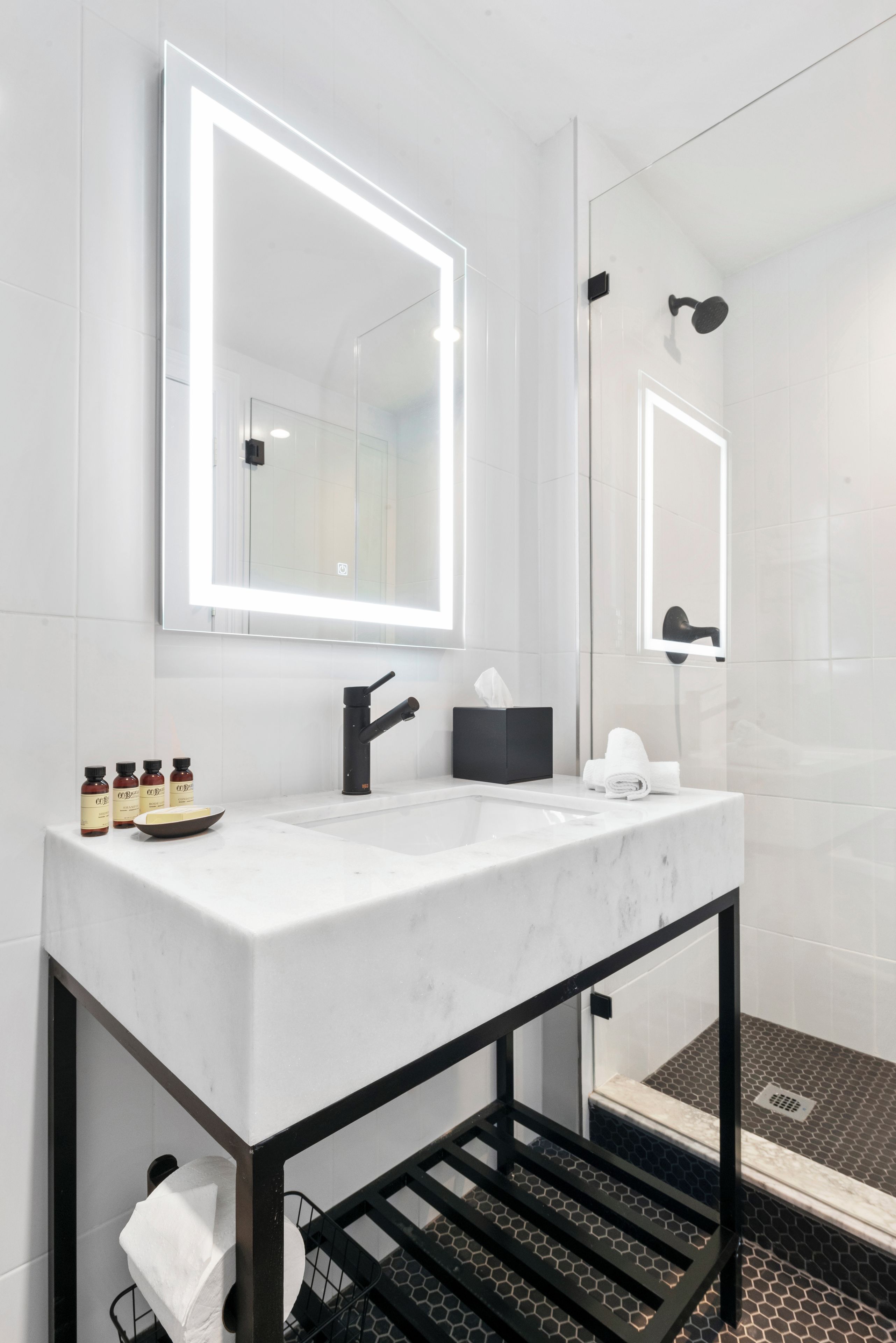 Une salle de bain moderne avec un lavabo en marbre blanc, des accessoires noirs et un grand miroir.