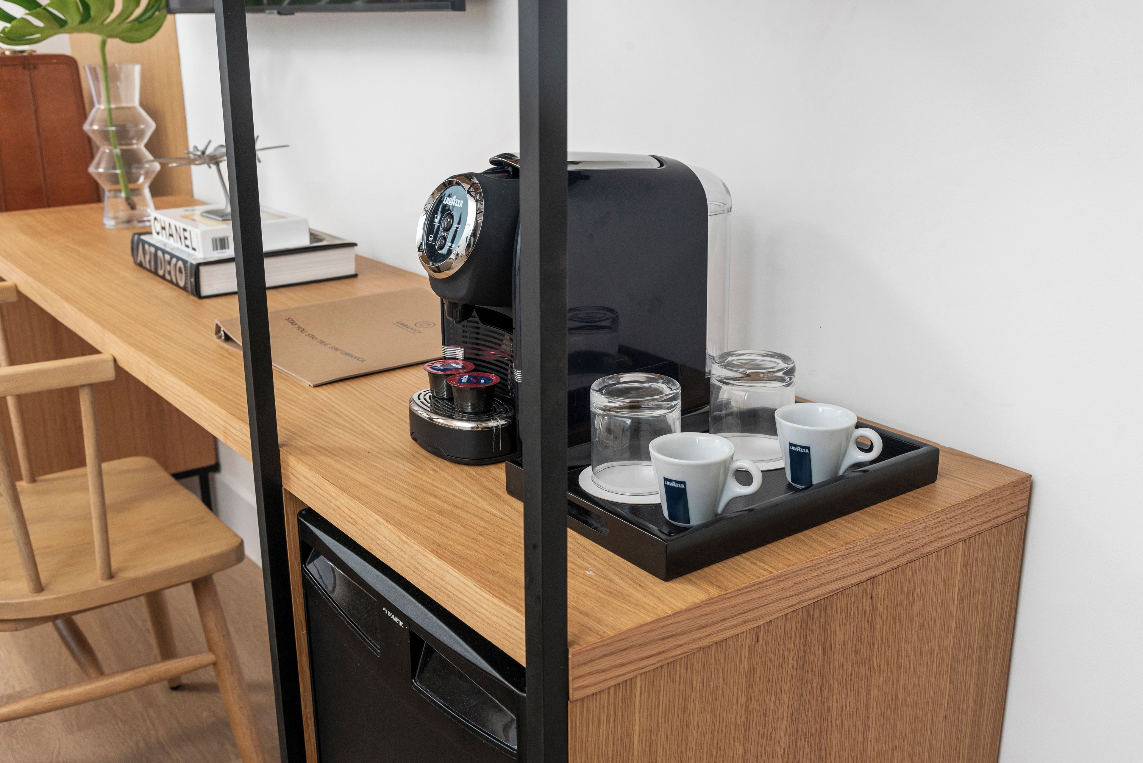 A compact kitchen area with a coffee machine, a tray with cups, and a book titled 'Art Deco'.