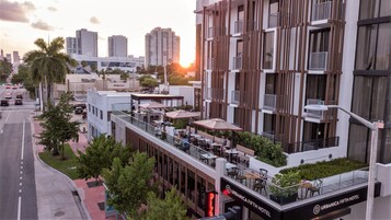 A modern hotel with outdoor seating, a visible restaurant, and a clear view of the city skyline.