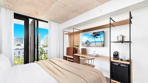 A modern hotel room with a large bed, a desk with a computer, a coffee machine, and a view of the city and beach. - UPSUN HOTEL (Miami Beach)