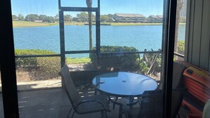 A view from a room with a glass door to a lake, a table with chairs, and a red chair. - LAKEFRONT~BEACH~GOLF~POOLS~TENNIS~PET FRIENDLY (Miramar Beach)