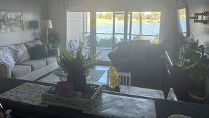 A living room with a sofa, a coffee table, a plant, and a view of a lake through large windows. - LAKEFRONT~BEACH~GOLF~POOLS~TENNIS~PET FRIENDLY (Miramar Beach)