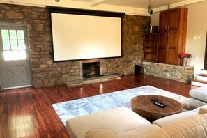 A living room with a stone fireplace, a large screen, and wooden cabinets.