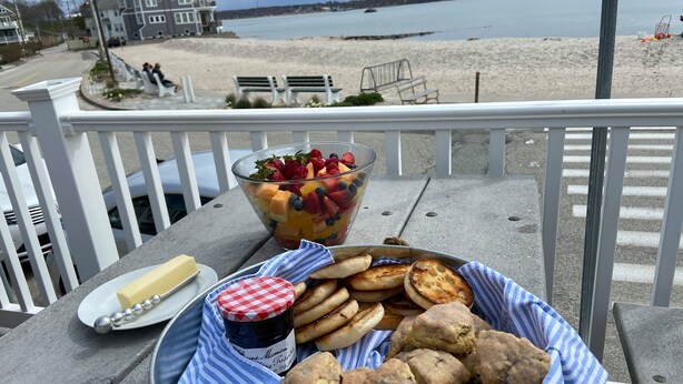 A table with a fruit salad, biscuits, butter, and jam on a balcony overlooking a beach. - Crescent Beach Cottage - Vacation or Academic Rental (Niantic)
